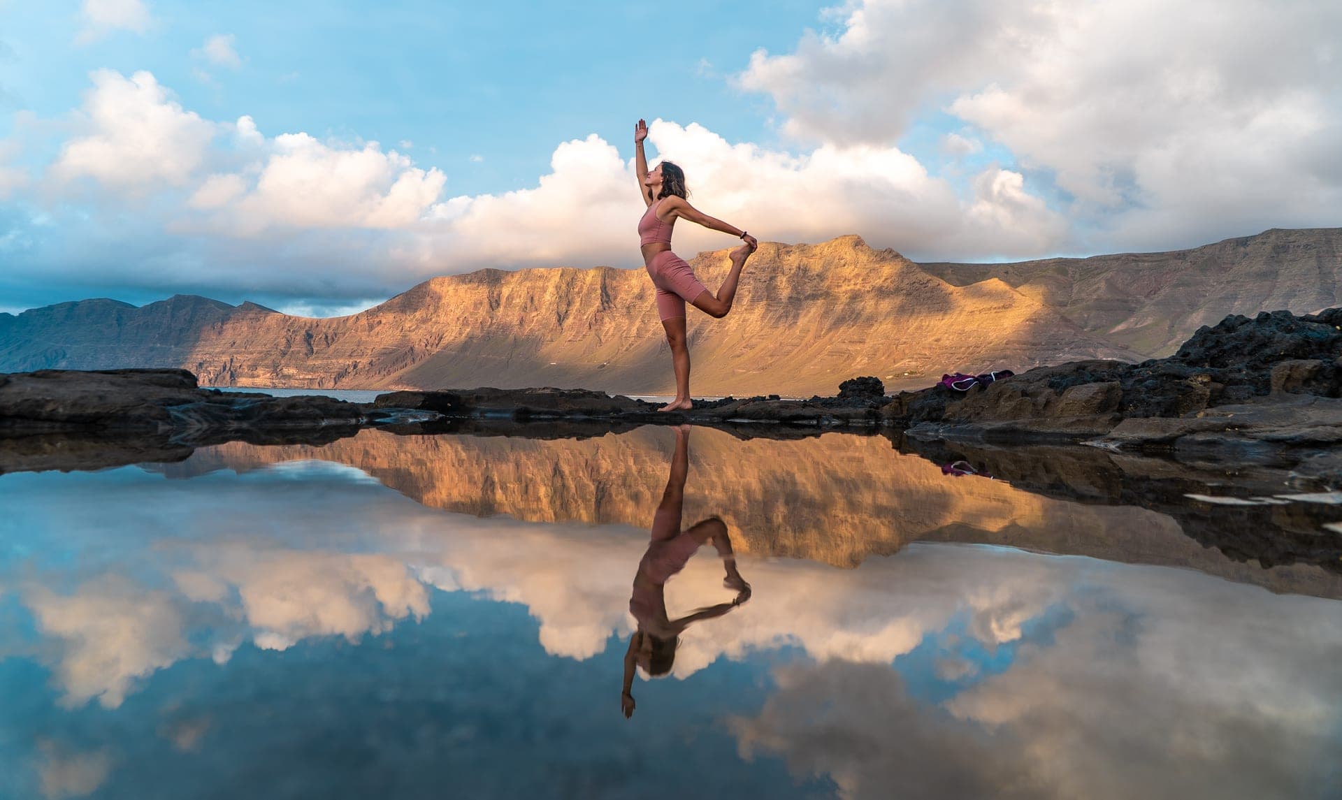 Donna in posizione yoga riflessa nell'acqua al tramonto, tra le montagne